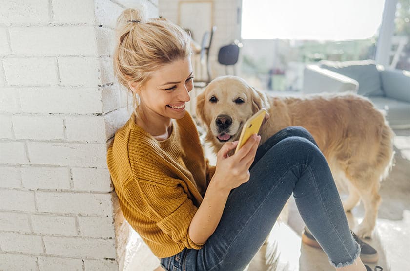 Happy woman on smartphone while her dog stands nearby