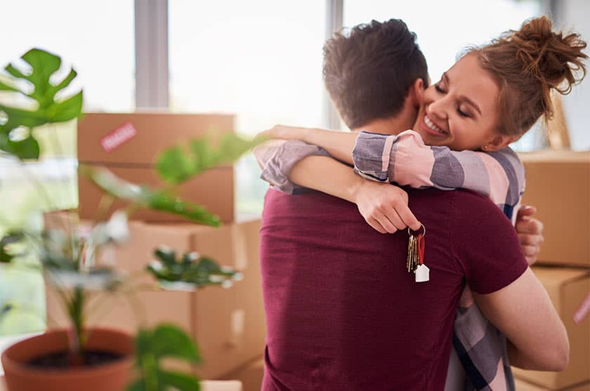 Couple hugging holding new home keys with moving boxes in background