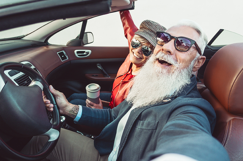 older couple wearing sunglasses in a convertible car taking a selfie and smiling