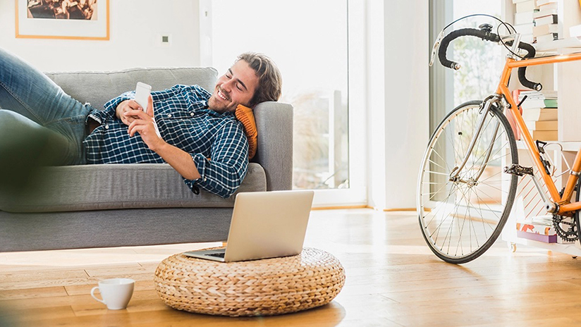 Man holding phone on couch next to laptop